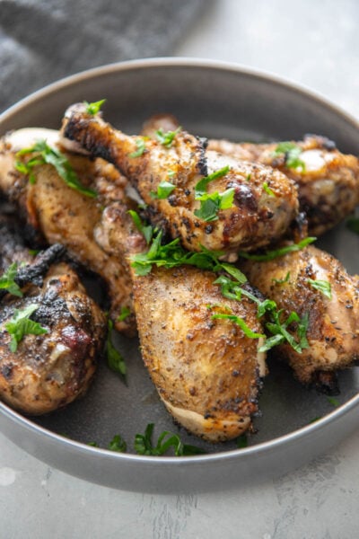 crispy chicken drumsticks topped with parsley in a gray bowl