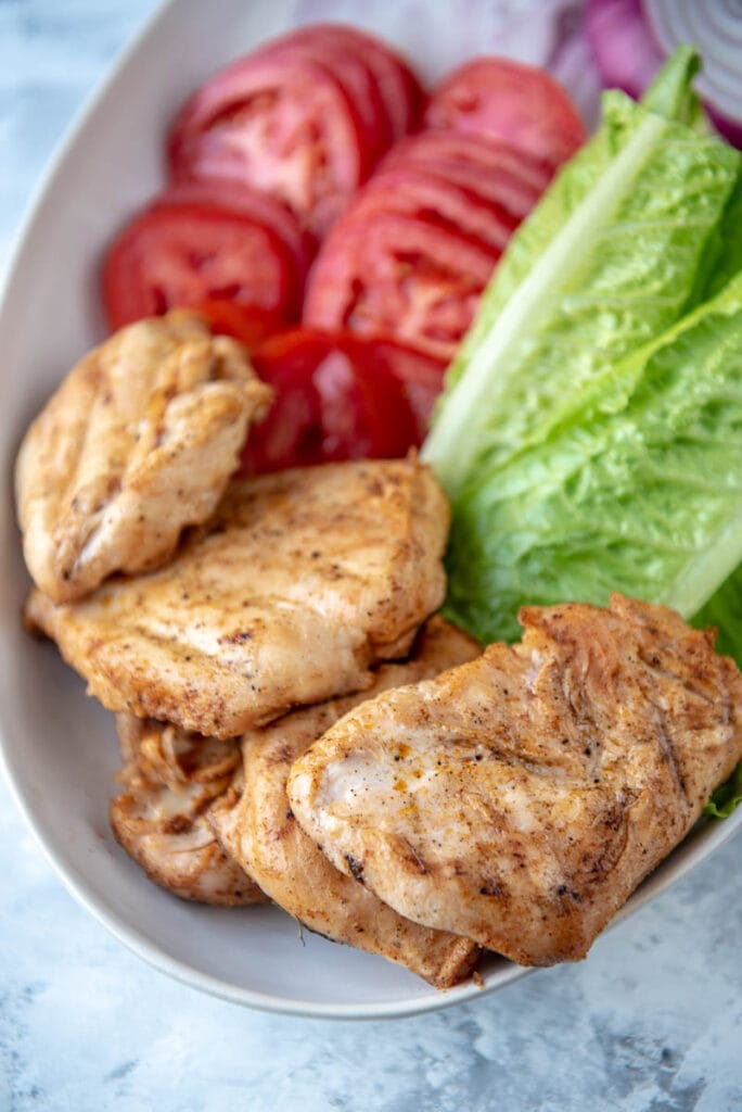white platter with grilled chicken, lettuce, tomato and onion