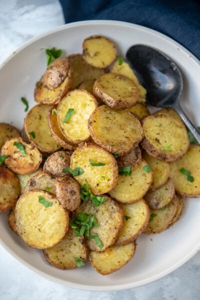 overhead view of sliced crispy grilled potatoes in a white bowl topped with chopped parsley