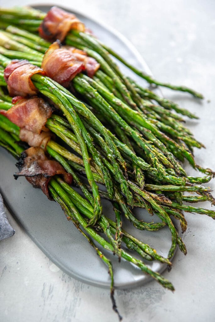 gray platter topped with grilled asparagus bundles wrapped in bacon
