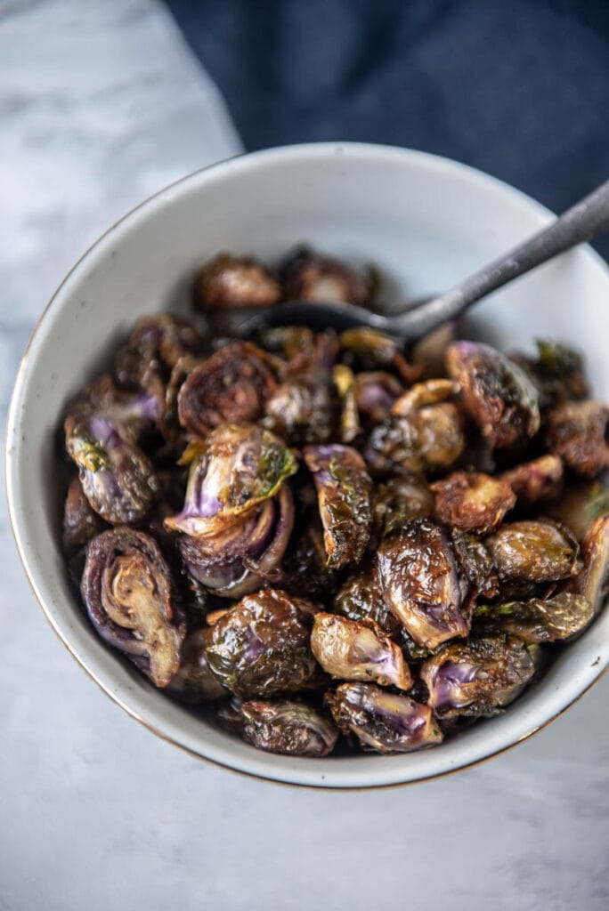 purple grilled Brussels sprouts in a white bowl with a gold rim