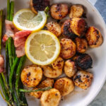 overhead shot of white bowl with grilled scallops on one side and bacon wrapped asparagus on the other