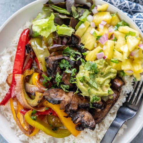 white bowl filled with rice topped with mushrooms, peppers, pineapple and guacamole