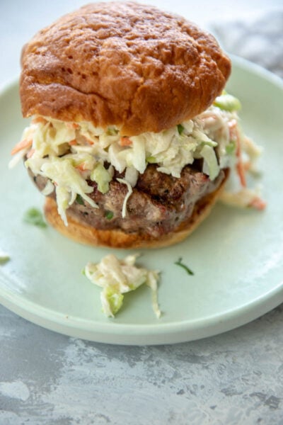 pork burger topped with slaw on gluten free bun on green plate