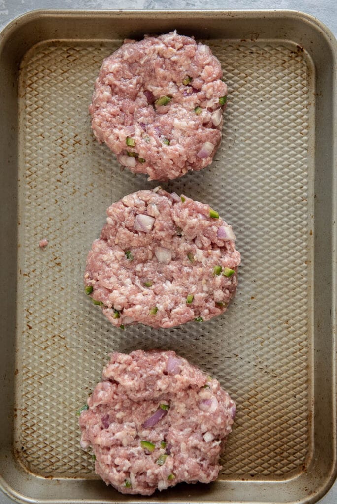 3 pork burger patties ready to cook on metal tray
