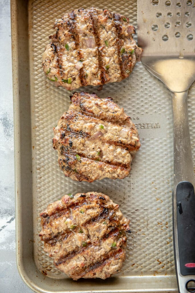 overhead view of 3 grilled pork burgers on a baking sheet with spatula