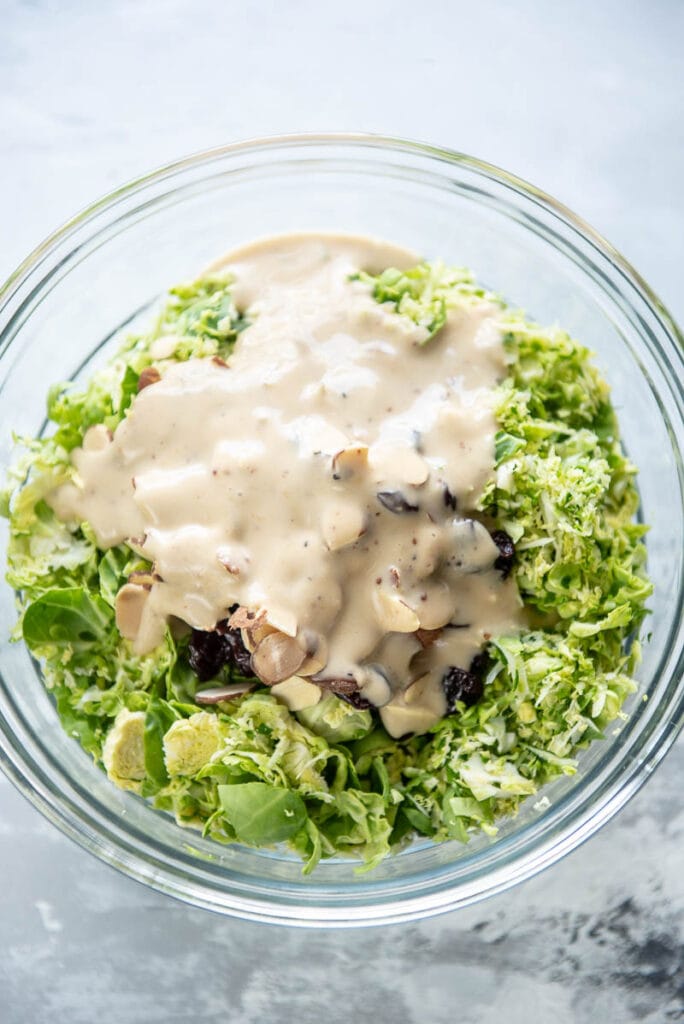 shredded brussels sprouts in bowl topped with honey mustard dressing