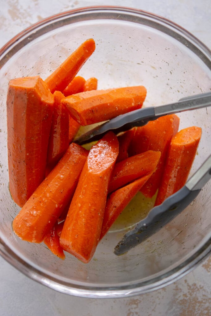 raw carrots in a glass bowl with thongs