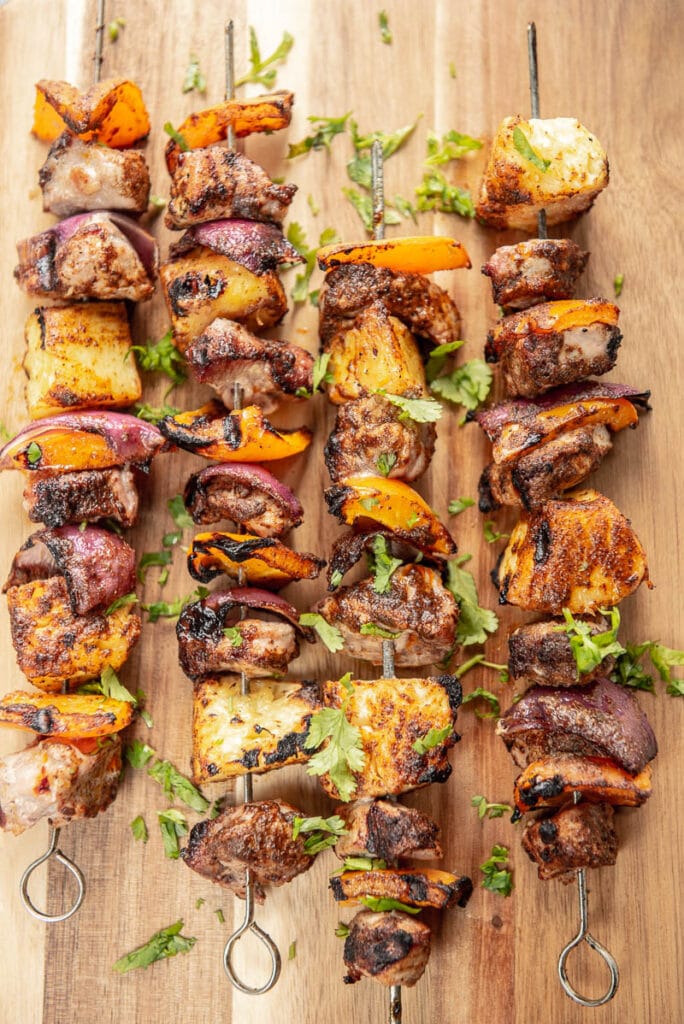 4 pork and veggie skewers on a wood board